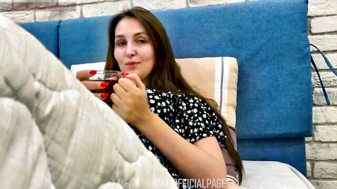 Brunette MILF in polka dot top sipping red wine on bed smiling seductively