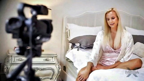 Blonde MILF Sophia West in pink lingerie robe, smiling seductively on bed