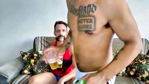 Muscular Latino studs in red tanks and briefs, one offering beer in teasing pose