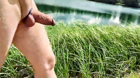 Nude man with cockring walking outdoors by lake, solo exhibitionism