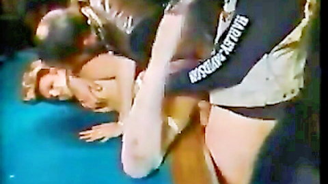 Blonde woman gangbanged by multiple men on blue mat with cock in pussy