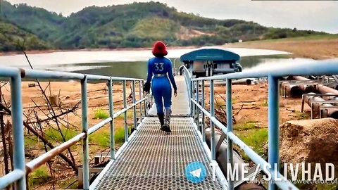 Redhead bimbo in tight blue superhero suit walking on pier by lake