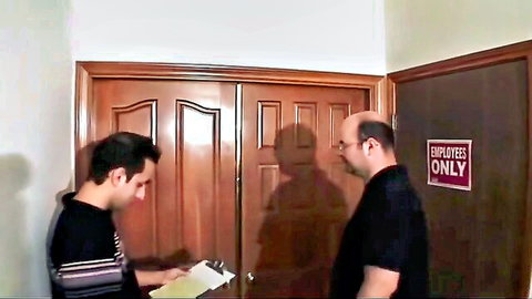 Two clothed men talking near employees only door with clipboard