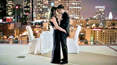 Casey Calvert in sensual rooftop kiss with suited man, black dress