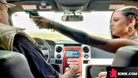 Tattooed man points gun at sexy tattooed woman's face in car BDSM tension