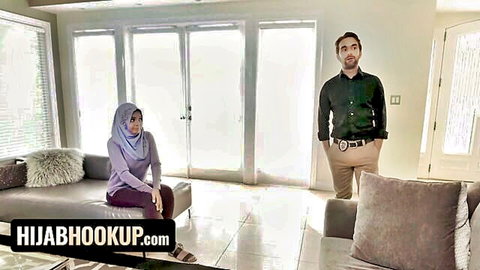 Aaliyah Hadid in hijab sits submissively on couch as man stands over her in tense scene