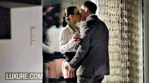 Brunette in blouse, skirt and stockings kisses suited man passionately