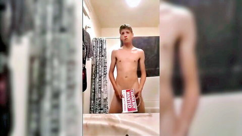 Slim young man nude in bathroom, holding wanted sign over crotch