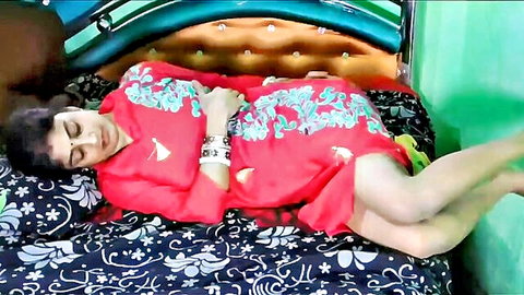 Curvy South Asian brunette in red embroidered dress lying seductively on bed with legs spread showing thighs