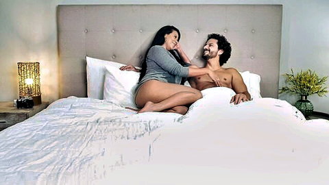 Tanned Latina brunette MILF in gray sweater straddles shirtless hunk kissing passionately on bed