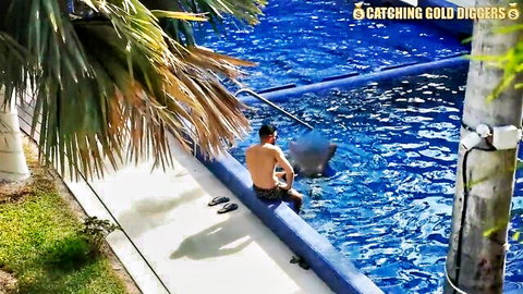 Shirtless man sits by tropical pool with manta ray, catching scene