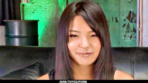 Cute Japanese teen with long black hair smiling seductively showing cleavage on leather couch