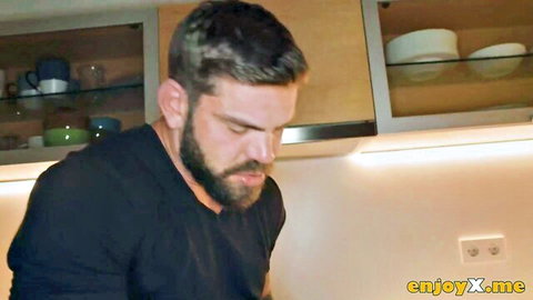 Bearded muscular man in black shirt bending down in modern kitchen