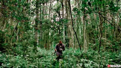 Armed man walks through dense green forest carrying rifle on shoulder