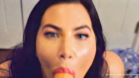 Korina Kova seductive close-up with orange in mouth, blue eyes gazing