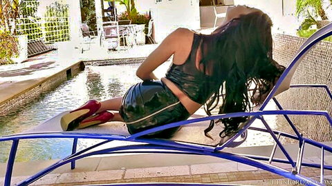 Curvy tanned brunette in shiny black latex shorts teasing big ass on poolside lounger