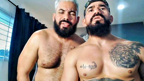 Two muscular bearded Latino men shirtless in intense close-up pose
