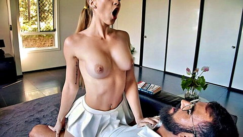 Topless blonde with perky tits and short skirt straddles bearded man in glasses, mouth agape in ecstasy