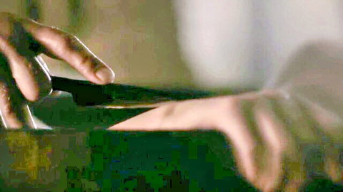 Hand gripping knife slicing into green vegetable in white bowl closeup