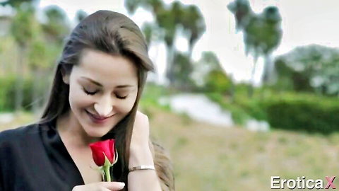 Sensual brunette in black dress smelling red rose outdoors