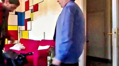 Two gay men in shirts stand by red couch with colorful abstract wall art