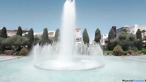 Fountain erupting tall white water jets into clear blue sky surrounded by palm trees and Las Vegas buildings