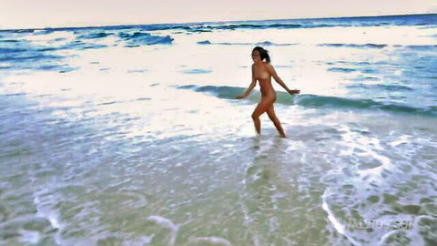 Curvy ebony woman topless walking in shallow ocean waves