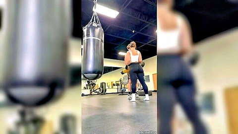 Fit athletic woman in tight leggings poses with punching bag in gym
