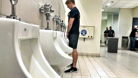 Blond guy standing at urinal in public bathroom, implied solo masturbation