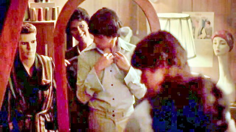 Vintage men in dress shop adjusting collars amid mirrors and mannequins, fully clothed.