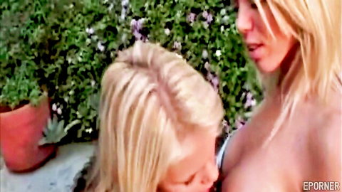 Busty blonde sucking another blonde's big exposed tits outdoors in garden