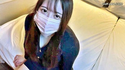 Masked Japanese beauty with seductive eyes teasing cleavage in unbuttoned blouse on bed