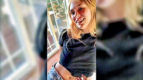 Smiling blonde woman in black crop top and jeans, showing midriff tease