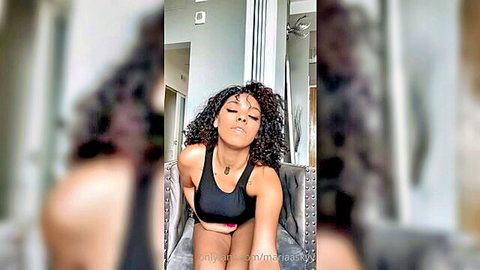 Curly-haired ebony woman in tight tank top showing cleavage, seductive pose
