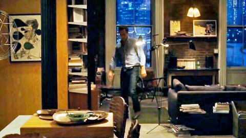 Handsome man in open shirt and jeans walks through stylish urban apartment at night