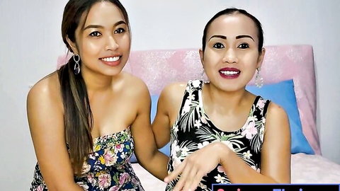 Two smiling Thai lesbian girlfriends in floral tank tops cuddling on bed
