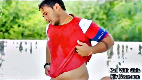 Indian man in wet red sports jersey lifting shirt to expose toned abs