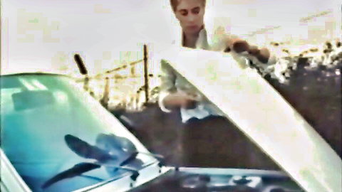 Blonde woman in white outfit leaning over open car hood outdoors