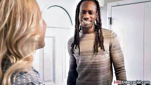 Blonde woman smiles at dreadlocked black man in sweater at doorway interracial tease