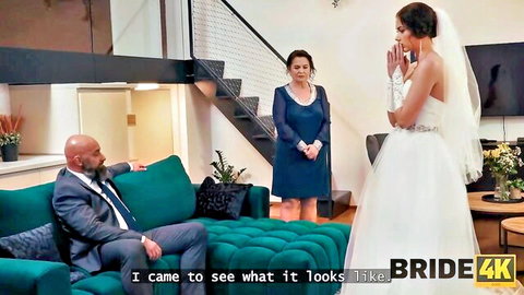 Bride in white wedding dress and veil stands nervously before bald man in suit on couch in cheating roleplay