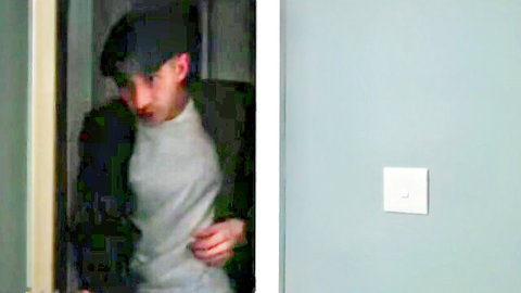 Man in black beanie and jacket stands in white doorway beside gray wall with white light switch