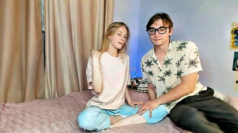 Blonde teen couple sits close on pink bed in casual webcam chat