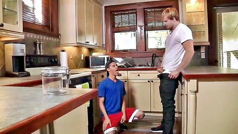 Two slim young men in kitchen, one kneeling orally pleasuring the redhead standing