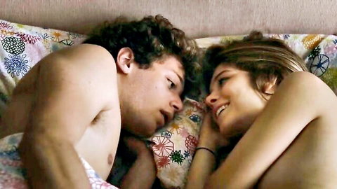 Naked young brunette smiling at shirtless curly-haired guy in intimate bed embrace