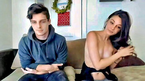 Amateur girlfriend topless beside boyfriend on couch, smiling seductively