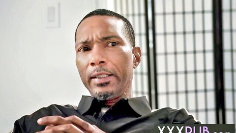 Intense Black man in open collar black shirt clasping hands seriously
