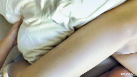 Young woman's pale legs spread wide gripping white bedsheet in bedroom tease
