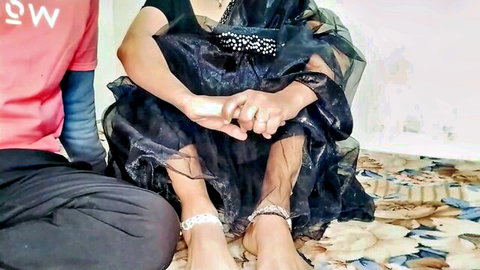 Sexy Indian woman in sheer black dress sits intimately with man holding hands on bed