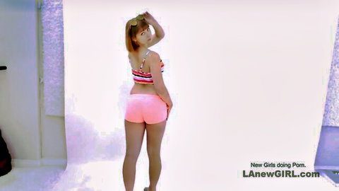 Cute Asian girl in tight pink shorts and striped top posing in studio