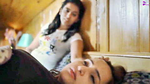 Busty Indian babe lying relaxed in t-shirt while friend leans nearby in wooden attic